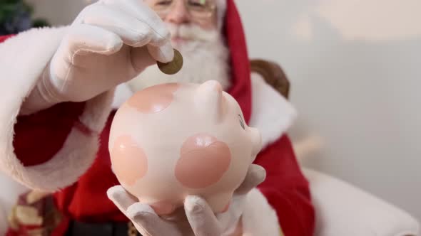 Santa Claus putting coin into a ceramic piggy bank. Savings concept for the end of the year.