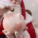 Santa Claus putting coin into a ceramic piggy bank. Savings concept for the end of the year. - VideoHive Item for Sale