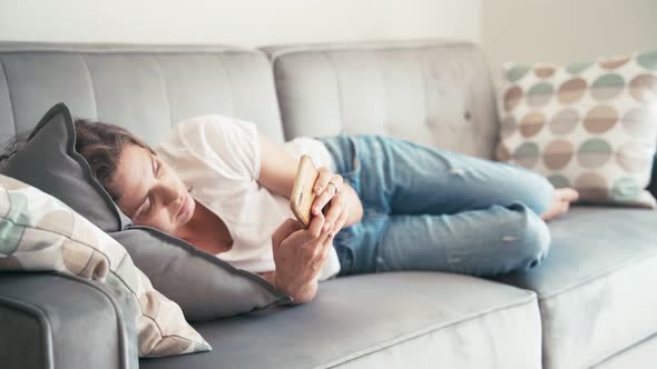 Serious Young Woman Lying on a Couch and Scrolling Websites on Her Smartphone