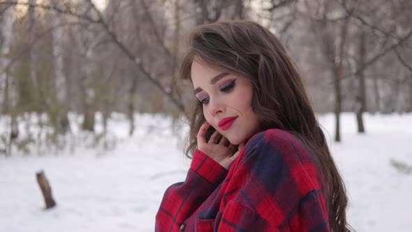 Young Woman with Wavy Hair Standing and Touching Face in Winter Forest