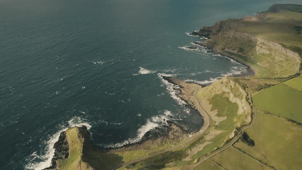 Aerial Ireland Bay Top Down: Green Rock Coast with Wide Grass Meadows, Fields and Rural Road