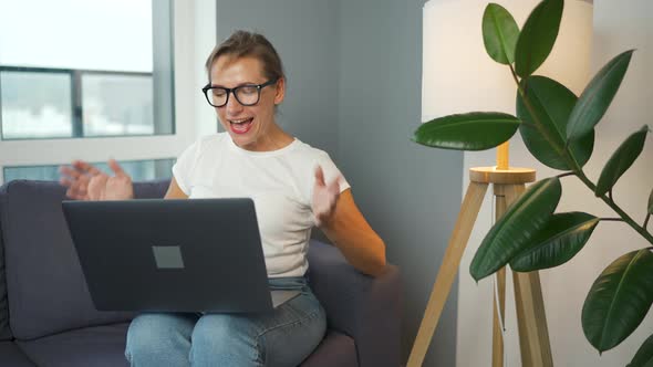 Casual Dressed Woman with Glasses Sitting on the Sofa and Communicates Via Video Link with Family or