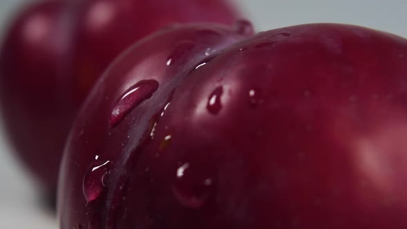 Drops of pure water splash and drip onto the textured surface of the ripe plum rind