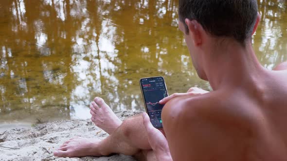 Male Relaxing on Beach Looks a Cryptocurrency Candlestick Chart in a Mobile App