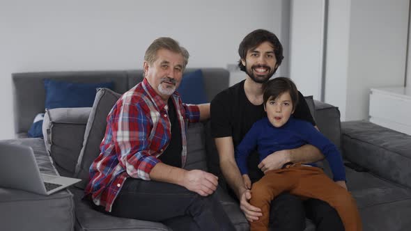 Portrait of Happy Caucasian Three Generation Men Smiling to the Camera at Home Sitting on Sofa