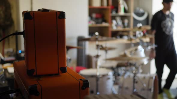 A drummer gets up from his instrument  during a rock and roll garage band practice with guitar amp a