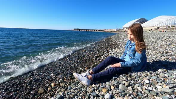 Girl Throws Stones Into Water and Jokes While Sitting on Sea Shore