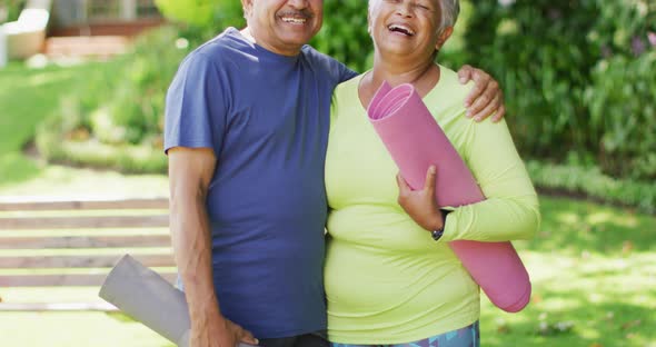 Video of happy biracial senior couple holding yoga mats and looking at camera in garden