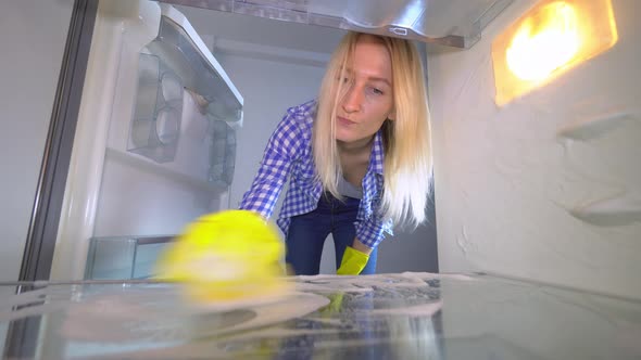 A disgruntled and irritated woman washes and cleans inside the refrigerator