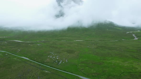 Pan up drone shot revealing Buachaille Etive Mor mountain peak hidden in white clouds in Scottish co
