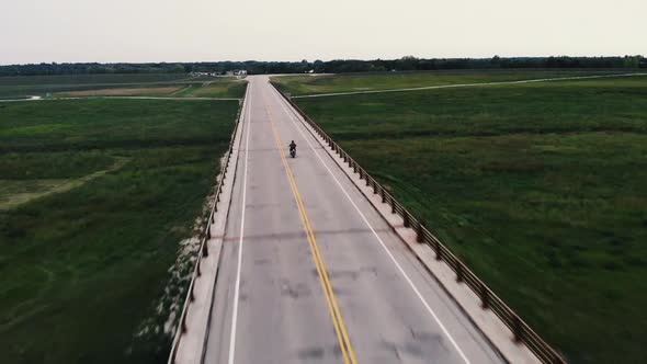 Drone shot of single motorcycle riding across bridge.