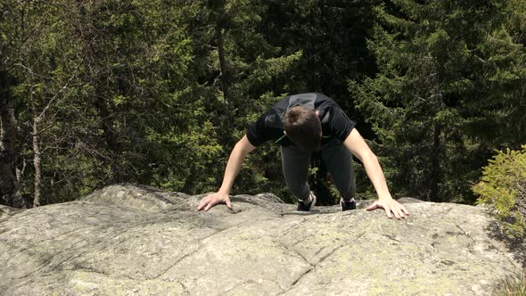 A tourist man climbs on a rock reached the top of the cliff