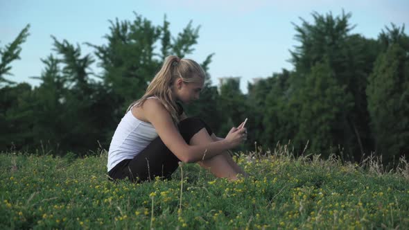 Young Girl Shirt Sits on a Hill and Gaining a Message on Your Mobile Phone.