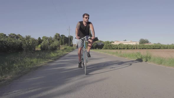 Cheerful man riding bicycle along rural field
