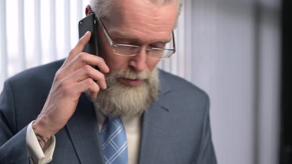 An adult gray-haired respectable man discusses business on the phone