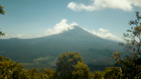 Aerial shot flies through opening in trees and up over a valley with Mount Agung in Bali in the dist