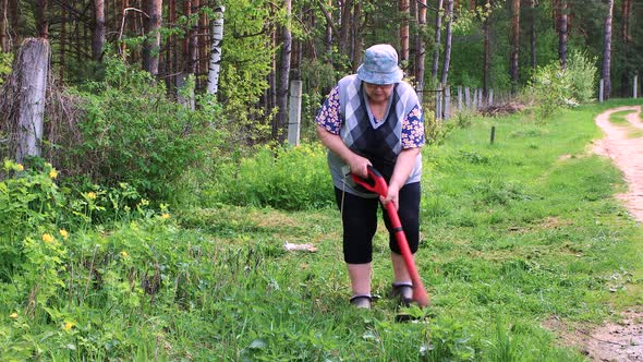 A Woman Mows Low Green Grass with an Electric Trimmer