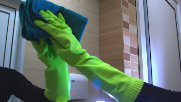 Woman in Green Gloves Cleans a Mirror in the Bathroom.