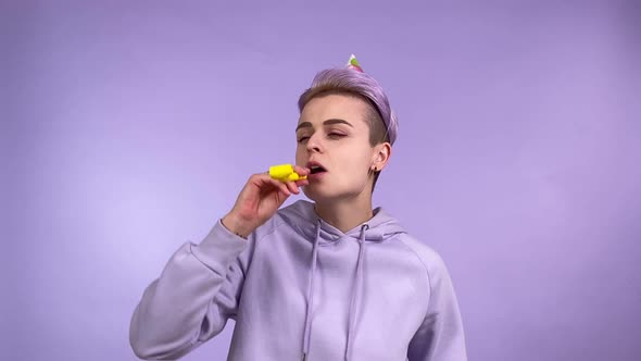 Young Woman Wearing Party Hat Blowing Party Horn Isolated on Purple