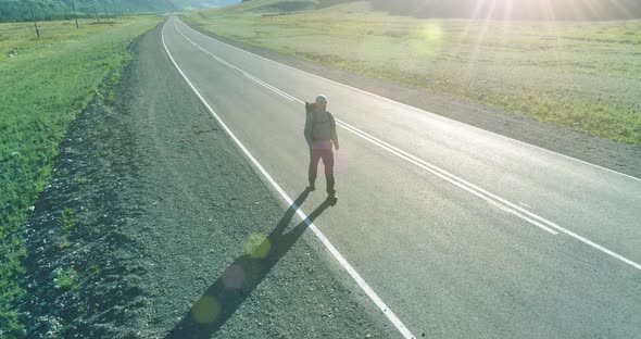 Flight Over Hitchhiker Tourist Walking on Asphalt Road. Huge Rural Valley at Summer Day. Backpack