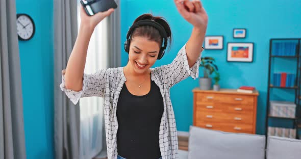 Smiling Woman Dancing in the Room Wireless Headphones on Ears Holding the Phone Waving Head