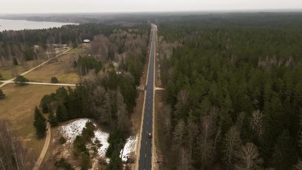 Ascending Aerial Shot Following Car Driving on Asphalt Road Between Forest Trees in Winter