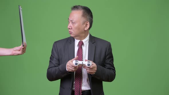 Mature Japanese Businessman Playing Games Against Green Background