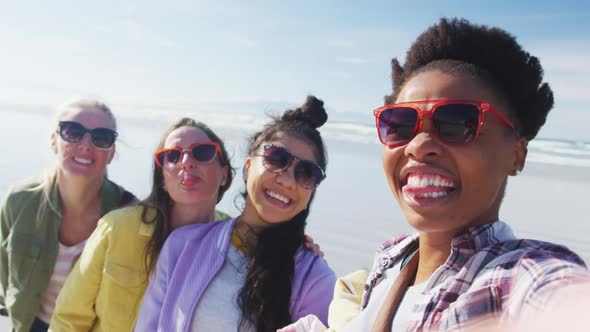 Happy group of diverse female friends having fun, taking selfie with smartphone at the beach