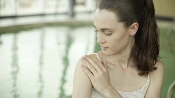 Woman applying moisturizer to shoulder in health spa