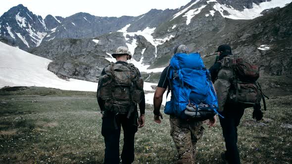 Well-equipped walkers go on rough terrain with high snow-capped mountains in the background