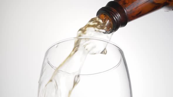 Beer is pouring with bubbles and foam in large beer glass from bottle on white background close up.