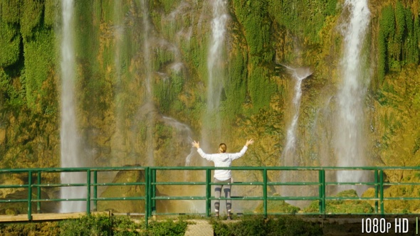 Woman Standing by Waterfall with Her Raised Hands