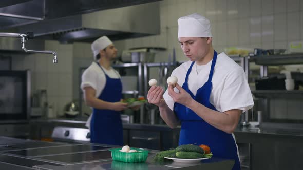 Serious Cook Checking Mushrooms in Slow Motion As Coworker Passing at Background with Vegetables