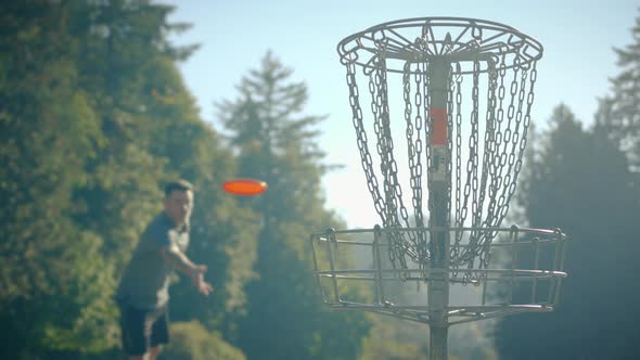 Man Throwing Disc Into Basket At Frisbee Golf Course