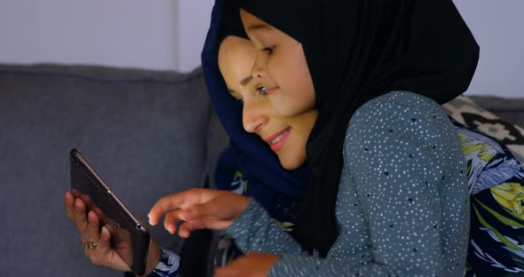 Mother and daughter using digital tablet in living room 