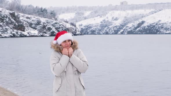 A Woman in Santa's Hat Walks Along the River in Nature in Winter Slow Motion