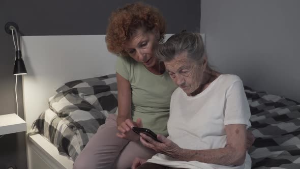 Happy Middle Aged Woman Hugs Senior Mom, Showing How To Use Mobile Apps. Smiling Elderly Mother