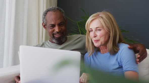 Mixed race senior couple using laptop while sitting on the couch at home