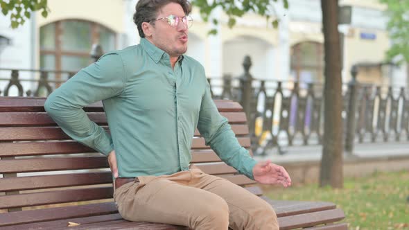 Man having Back Pain while Sitting on Bench