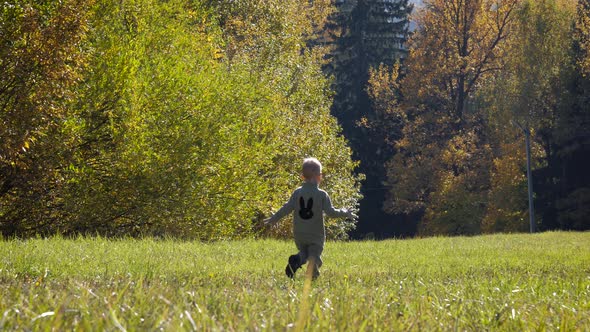 Funny Small Child Runs Down Slide On Green Field On Autumn Sunny Day