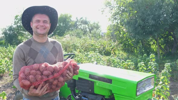 Farmer Inspects the Potato Harvest on the Background of a Green Tractor