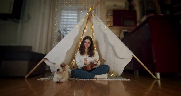 The Girl Sits in a Children's Tent with a Dog Jack Russell and Plays the Guitar