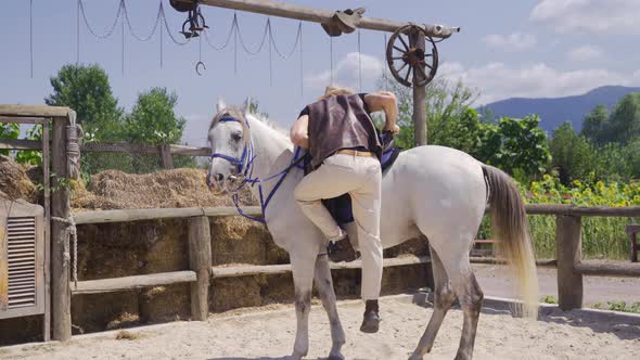 The man riding his horse on the farm. Attractive white horse.