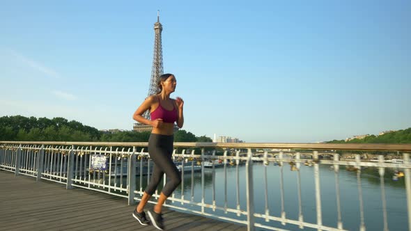 A woman running across a bridge with the Eiffel Tower