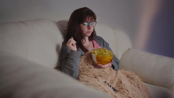 Happy Pretty Woman with Glasses Watching Tv in the Evening Eating Chips and Smiling