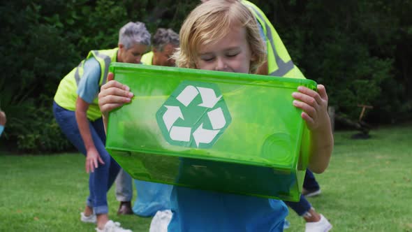 Smiling caucasian boy holding recycling box picking up litter with volunteers in field