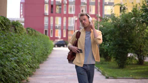 Positive, young man walks down the street in headphones, listens to music