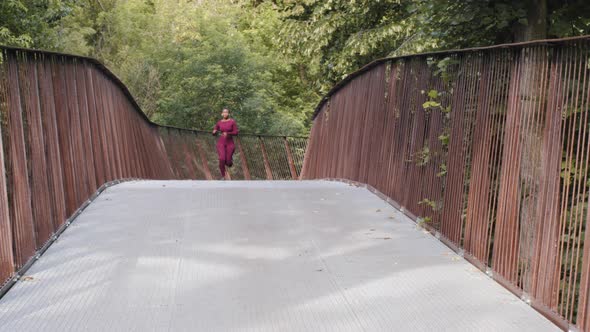 Young Athletic Beautiful Ethnic Female in Activewear Running on Bridge During Everyday Practice