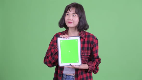 Happy Asian Hipster Woman Thinking While Showing Digital Tablet