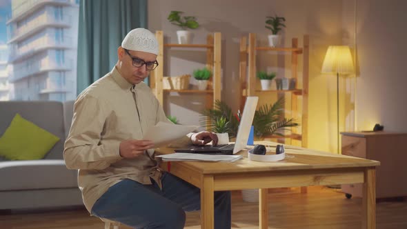 Muslim Man in a Skullcap Works From Home with a Laptop